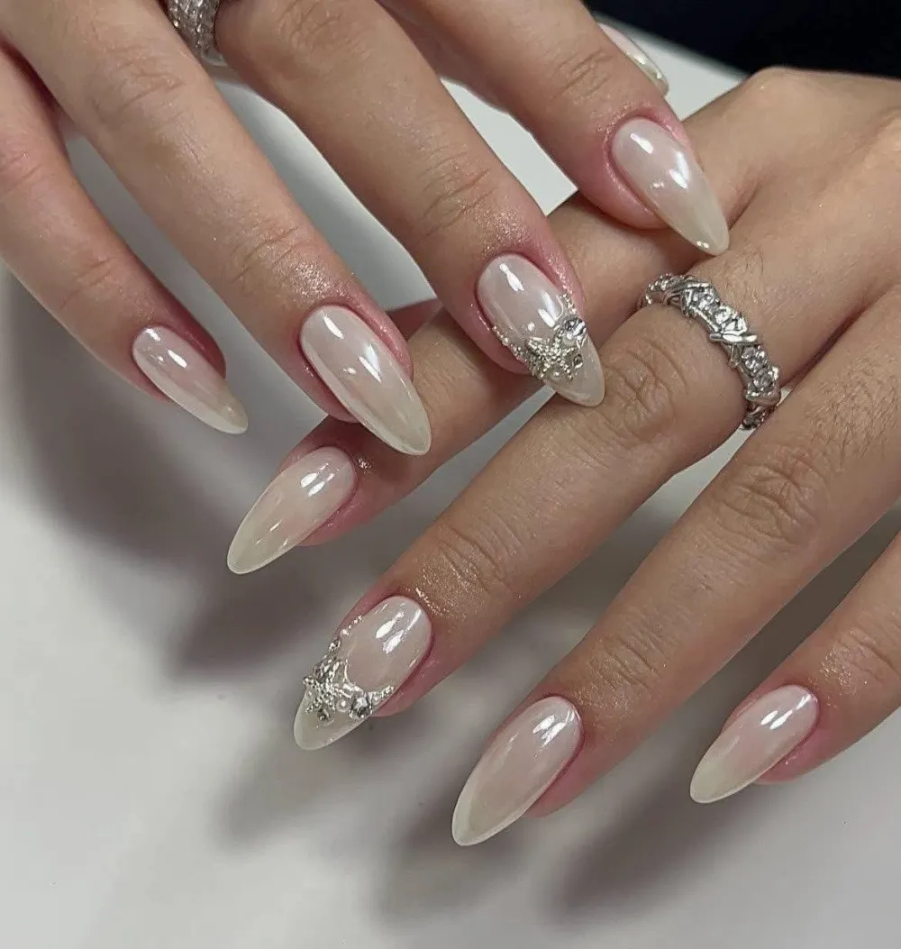 Milky pearl-chrome almond nails with silver star and rhinestone accents.